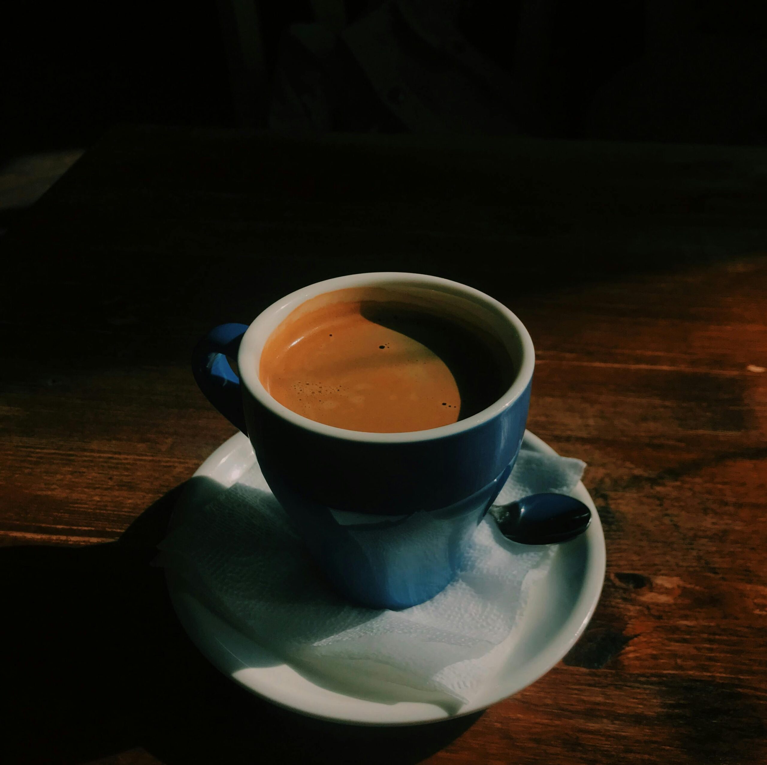 A warm cup of coffee in a blue mug on a wooden table, capturing a cozy cafe ambiance.