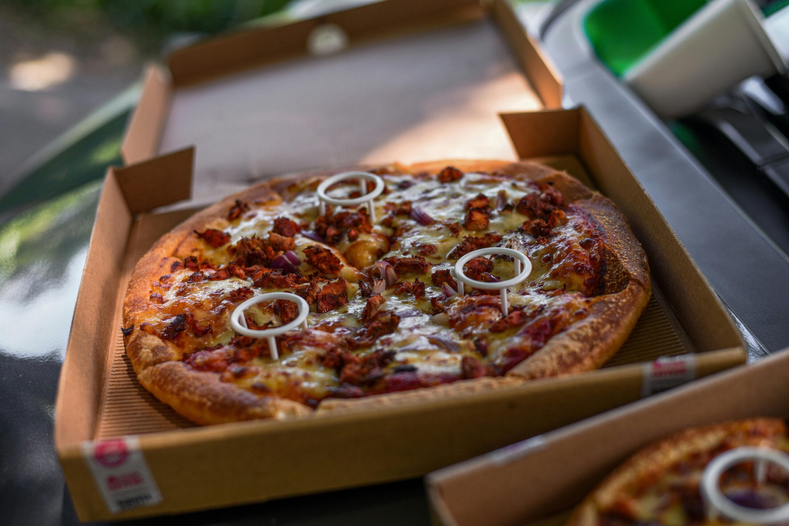 Close-up of a freshly baked pizza with toppings in a cardboard box, mouthwatering and ready to eat.